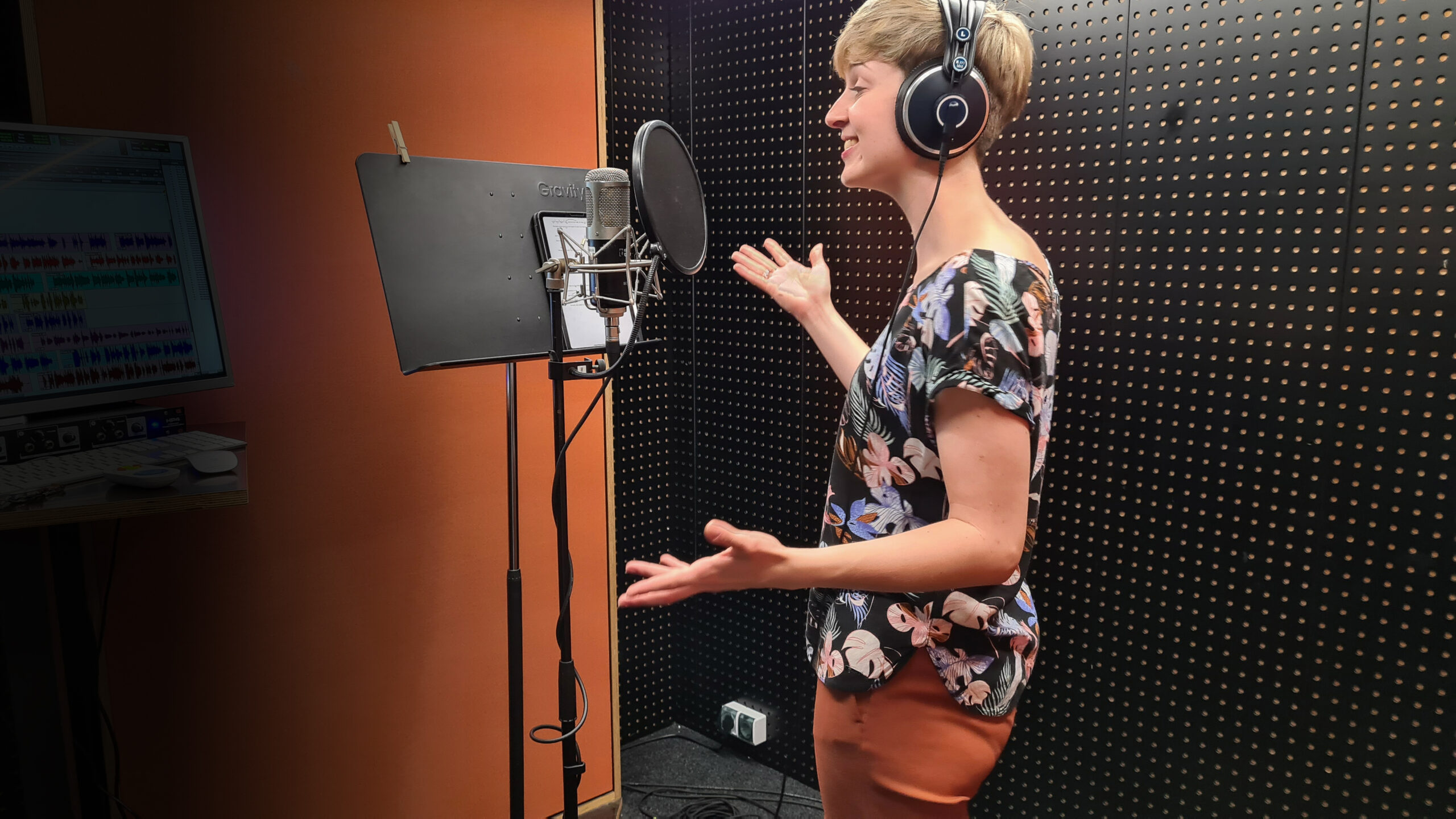 Carolin Schmidt steht lächelnd und mit ausgebreiteten Armen im Studio vor dem Mikrofon. Dabei trägt sie Kopfhörer.